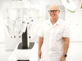 Přednosta chirurgické kliniky Lukáš Sárka v popředí, chirurgický robot da Vinci v pozadí.